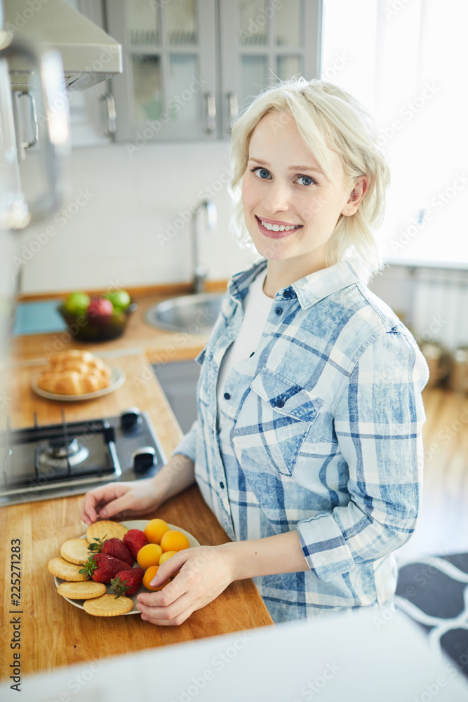 Young woman preparing fresh fruits and crackers for breakfast in the kitchen