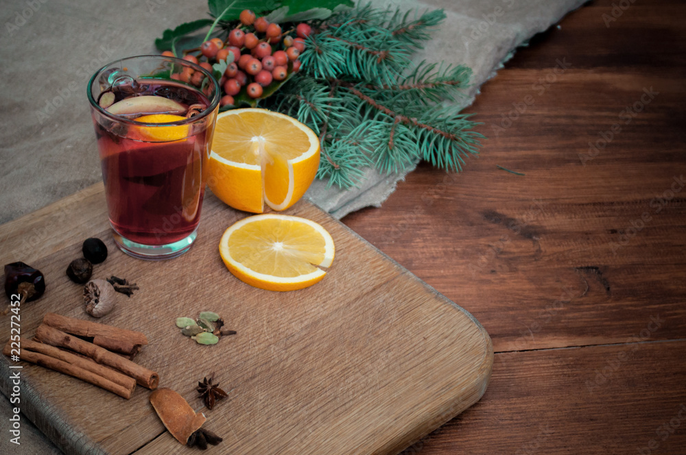 Angle view mulled wine with citrus, cinnamon, cardamon and anise spices and fir. Christmas cozy still life on wooden rustic background.