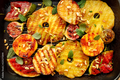 Grilled fruit; pineapples, peaches, figs, pears and watermelon with pine nuts, fresh herbs and honey on the grill plate, top view. Gourmet fruit dessert photo