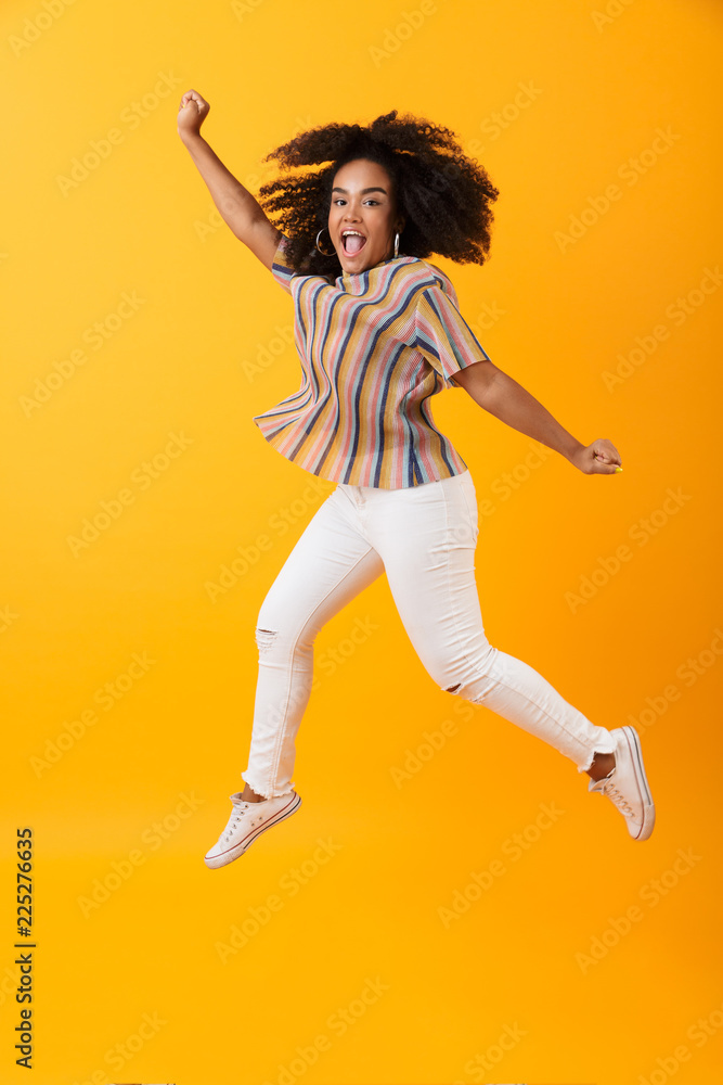 Emotional pretty african woman jumping isolated over yellow background.