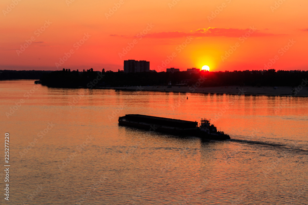 Tugboat pushing a heavy long barge on the river Dnieper at sunset