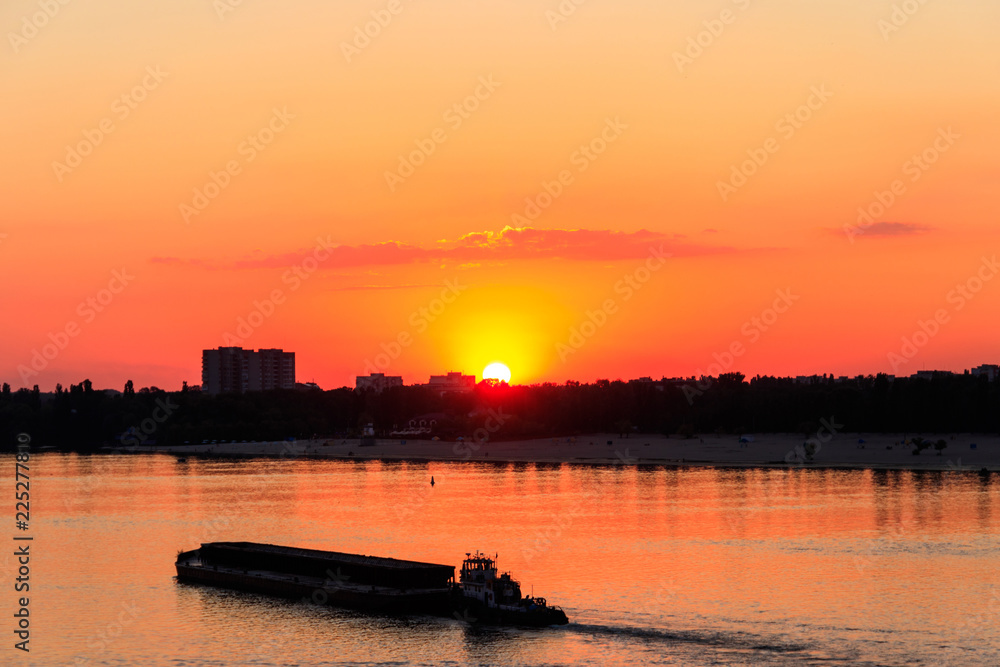 Tugboat pushing a heavy long barge on the river Dnieper at sunset