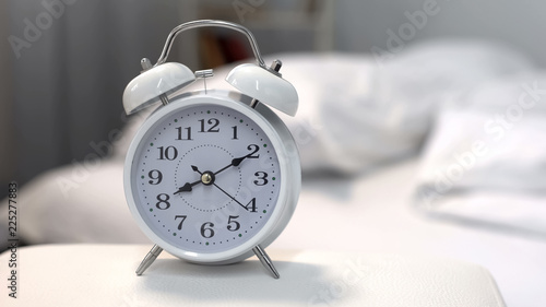 Alarm clock showing morning time on night table near bed, sleeping hours