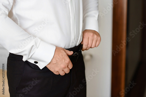 Grooms morning preparation, handsome groom getting dressed and preparing for the wedding, wearing a belt