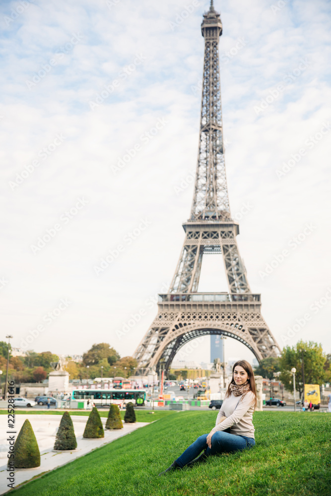 Attractive young lady sist on grass. Background of eiffel tower