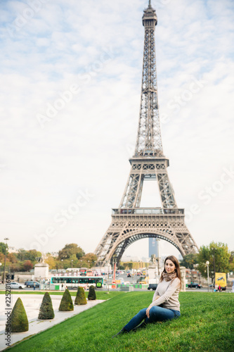 Attractive young lady sist on grass. Background of eiffel tower © Aleksandr