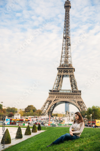 Attractive young lady sist on grass. Background of eiffel tower © Aleksandr