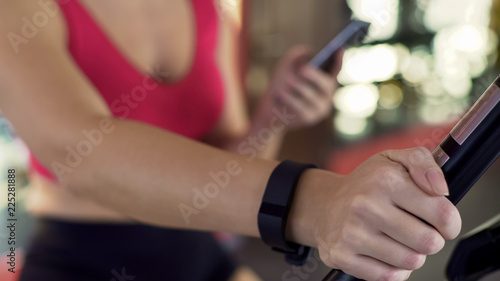 Fitness bracelet on womans hand, athletic girl riding exercise bike, closeup