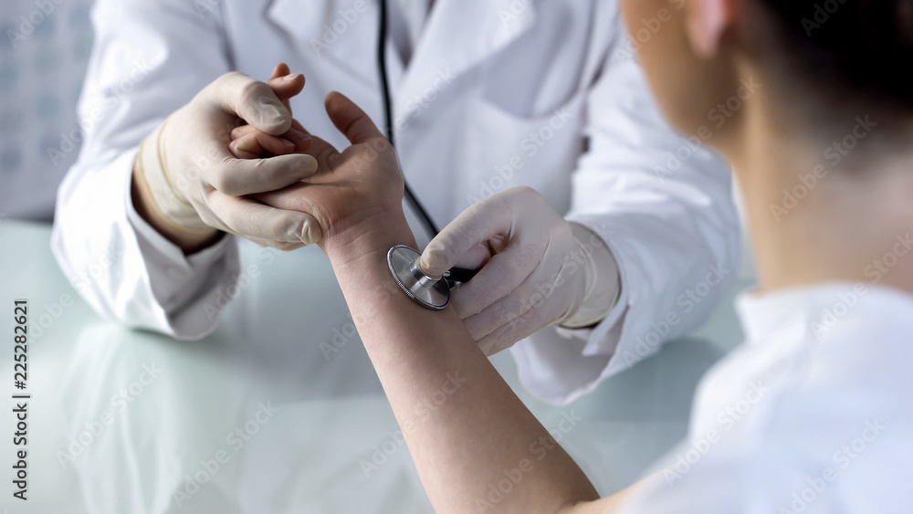 Physician examining females pulse with stethoscope, hospital appointment, health Physician examining females pulse with stethoscope, hospital appointment, health