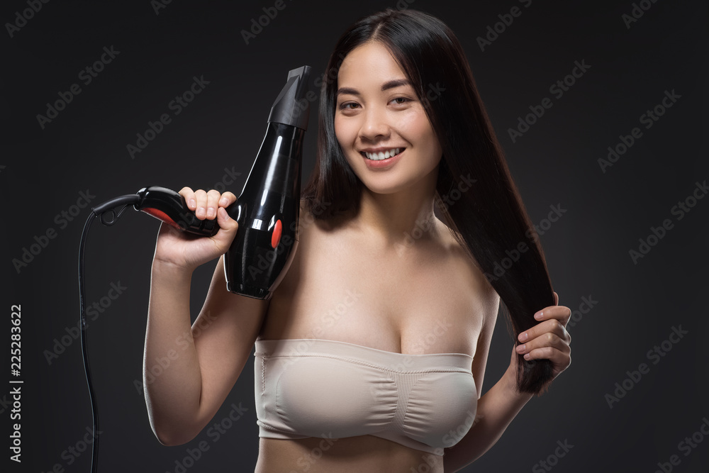 portrait of smiling asian woman with hair dryer looking at camera isolated on black portrait of smiling asian woman with hair dryer looking at camera isolated on black