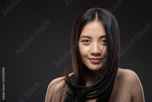 portrait of young smiling asian woman with beautiful and healthy dark hair looking at camera isolated on black