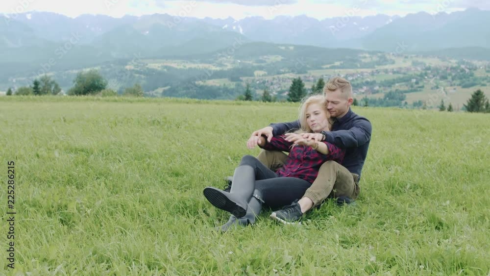 Couple sitting and kissing on grass on the top of mountains enjoying mountains and clouds landscape. Love and travel concept. Lifestyle concept. family active traveling. Mountain view Couple sitting and kissing on grass on the top of mountains enjoying mountains and clouds landscape. Love and travel concept. Lifestyle concept. family active traveling. Mountain view