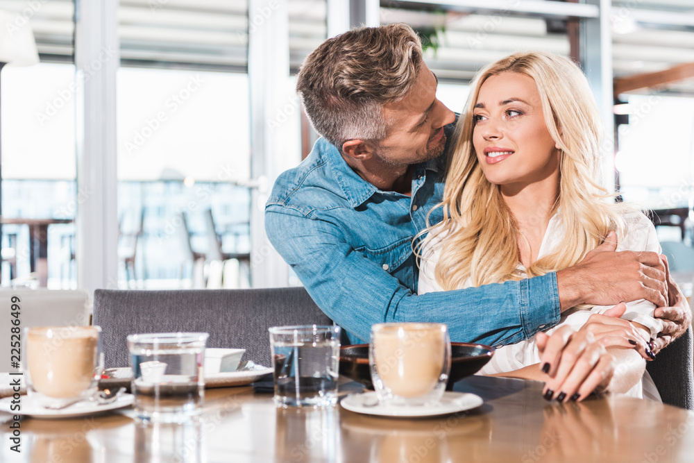 handsome boyfriend cuddling attractive girlfriend at table in cafe handsome boyfriend cuddling attractive girlfriend at table in cafe
