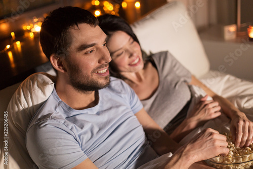 people, family and leisure concept - couple with popcorn watching tv at night at home