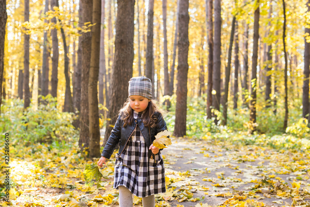 Autumn, seasons and children concept - happy little girl laughing and playing with fallen leaves in park
