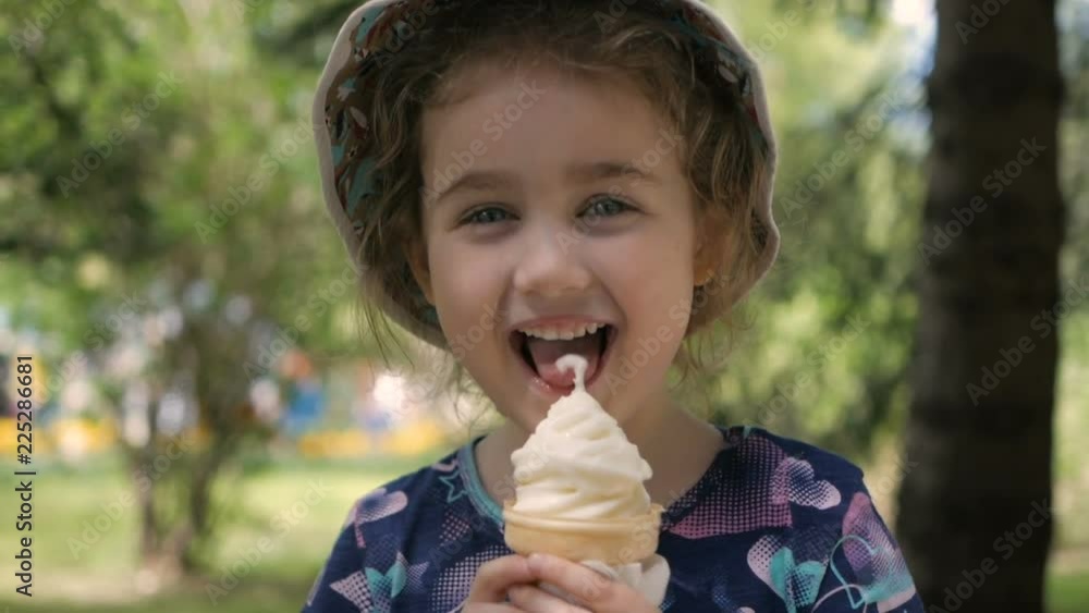 A cute little girl enjoys a delicious ice cream cone during the summer. Child with ice cream on a walk in the city park A cute little girl enjoys a delicious ice cream cone during the summer. Child with ice cream on a walk in the city park
