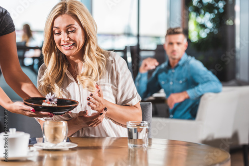 surprised happy woman looking at dessert with flower in cafe