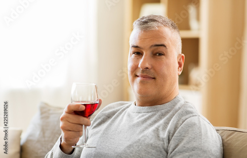 people, alcohol and drinks concept - man drinking red wine from glass at home