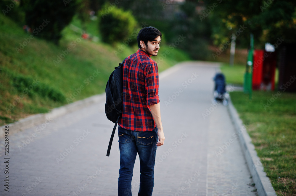 Young indian student man at red checkered shirt and jeans with backpack posed at street. Young indian student man at red checkered shirt and jeans with backpack posed at street.