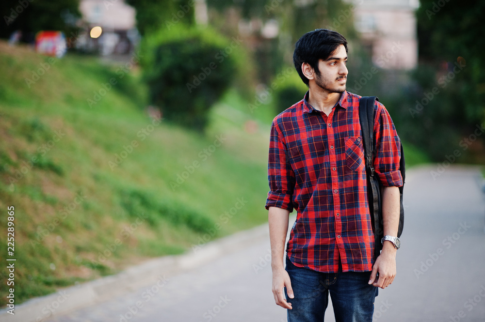 Young indian student man at red checkered shirt and jeans with backpack posed at street. Young indian student man at red checkered shirt and jeans with backpack posed at street.