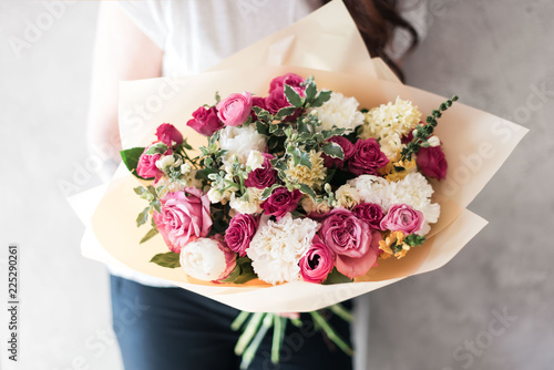 Fototapeta Naklejka Na Ścianę i Meble -  Very nice young woman holding blossoming flower bouquet of fresh roses, ranunculus, eustoma, eucalyptus in pink colors on the grey wall background