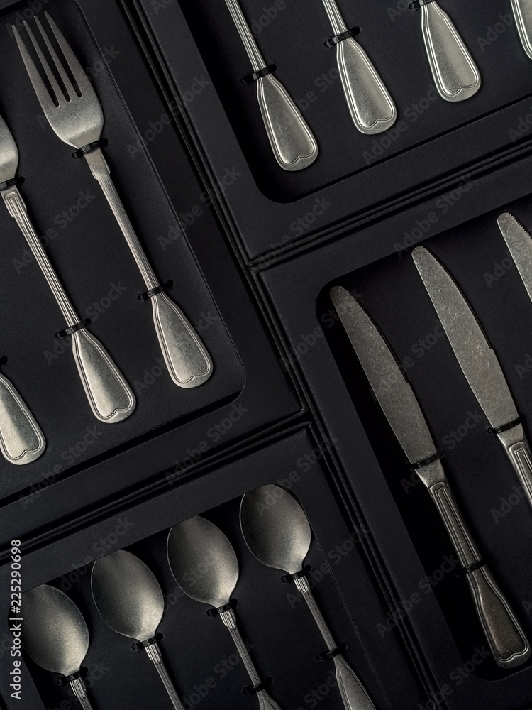 Top view of silver collection of knives forks spoons tablespoons and teaspoons in a black box on a gray concrete background Top view of silver collection of knives forks spoons tablespoons and teaspoons in a black box on a gray concrete background