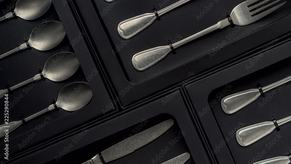 Top view of silver collection of knives forks spoons tablespoons and teaspoons in a black box on a gray concrete background Top view of silver collection of knives forks spoons tablespoons and teaspoons in a black box on a gray concrete background