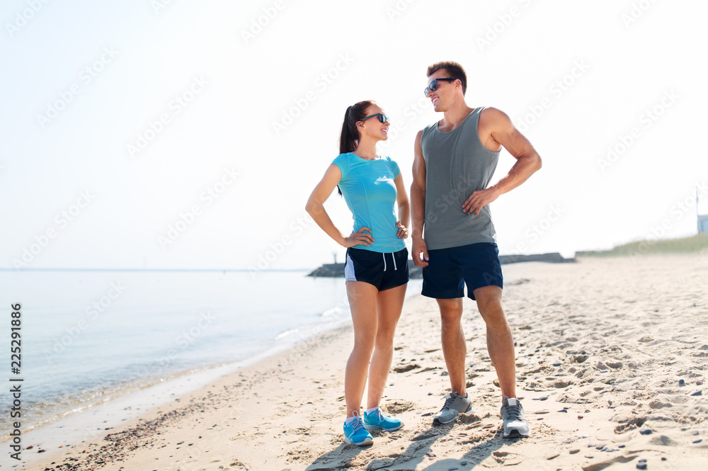 fitness, sport and lifestyle concept - happy couple in sports clothes and sunglasses on beach
