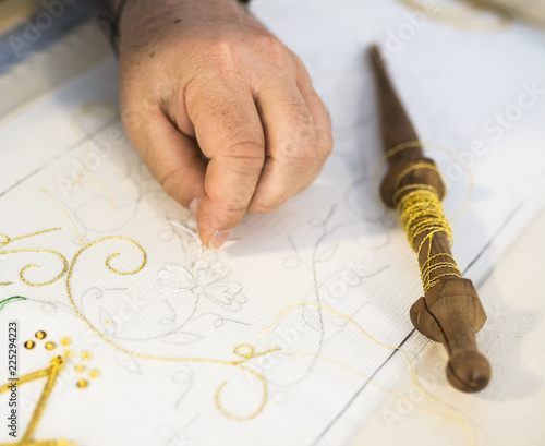 Detail of a man's hands embroiderer with a sewing thread on.Details of embroiderywith gold-colored thread