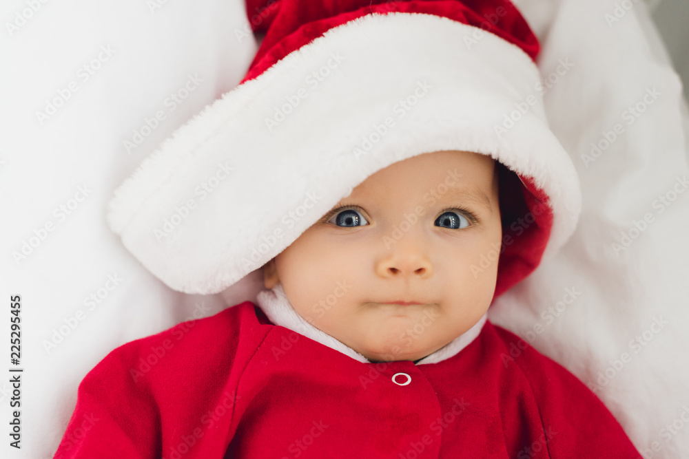 close-up portrait of adorable little baby in santa suit lying in bed and looking at camera close-up portrait of adorable little baby in santa suit lying in bed and looking at camera