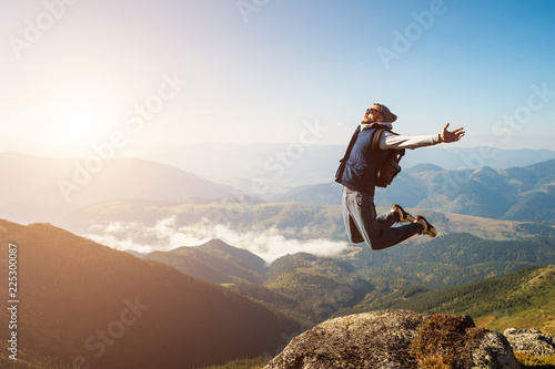 Young man jumping on top of a mountain against the sky photo