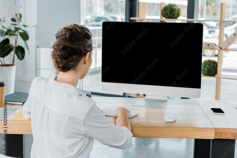 back view of businesswoman working on computer with blank screen in office