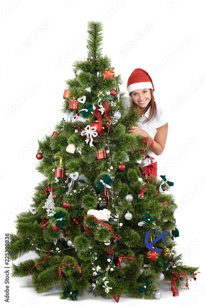 Beautiful smiling woman in Santa cap, behind the Christmas tree, isolated on white Beautiful smiling woman in Santa cap, behind the Christmas tree, isolated on white