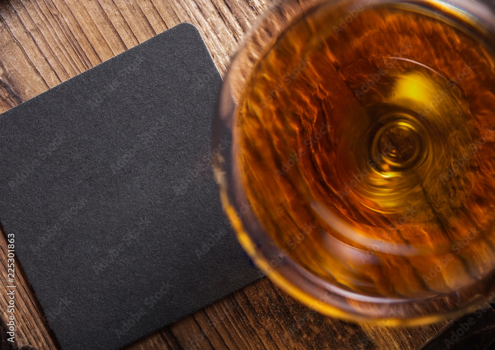 Glass of cognac brandy drink with black coaster on top of wooden barrel.
