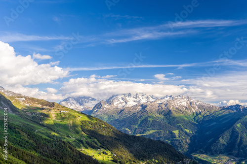 Scenic view of beautiful landscape in Swiss Alps. Fresh green meadows and snow-capped mountain tops in the background in springtime, Switzerland.
