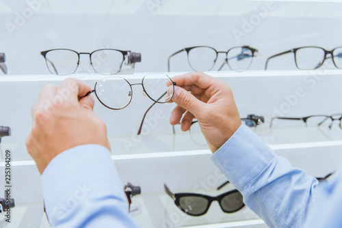 cropped image of man taking eyeglasses from shelves in ophthalmic shop