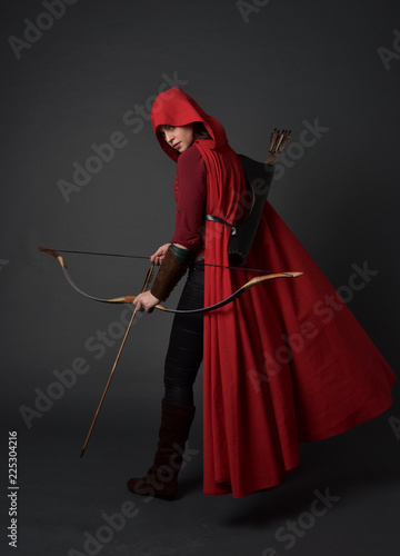 Принти на полотні full length portrait of brunette girl wearing red medieval costume and cloak, holding a bow and arrow