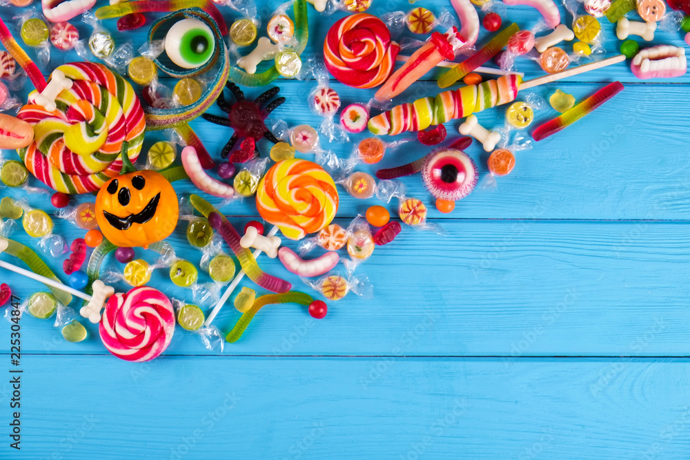 Assorted teeth and eyeball shaped candy spread on wooden table, jelly spider, gummy worms, round lollipop and other mixed candy on blue wood background. Top view, copy space, close up, flat lay.
