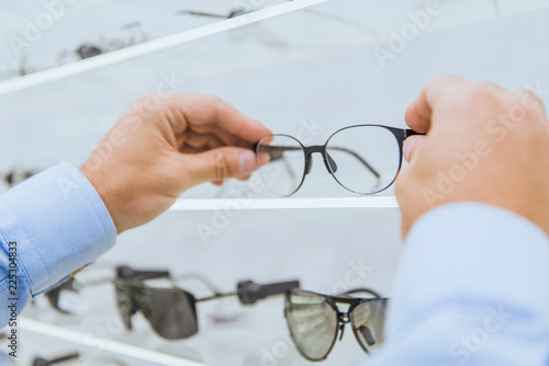 cropped view of person taking eyeglasses from shelf in optica
