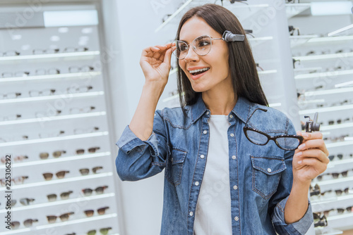 smiling attractive woman choosing eyeglasses in optics