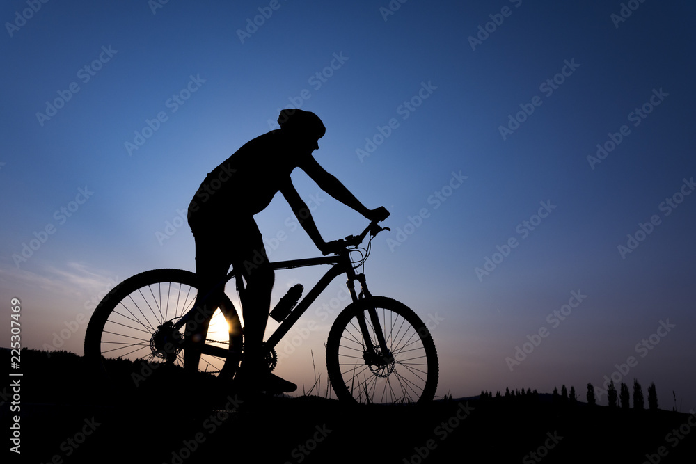 Obraz premium Silhouette of boy on the bike. Young cyclist is jumping on his bike during sunset.
