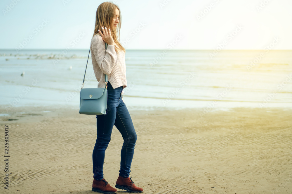 Beautiful woman in a jeans sweater shoes female bag watch on a nature background sun Beautiful woman in a jeans sweater shoes female bag watch on a nature background sun