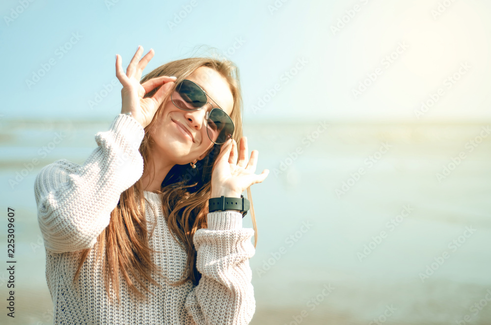 Woman holds sunglasses on the background of the sea sun sweater watch autumn cold