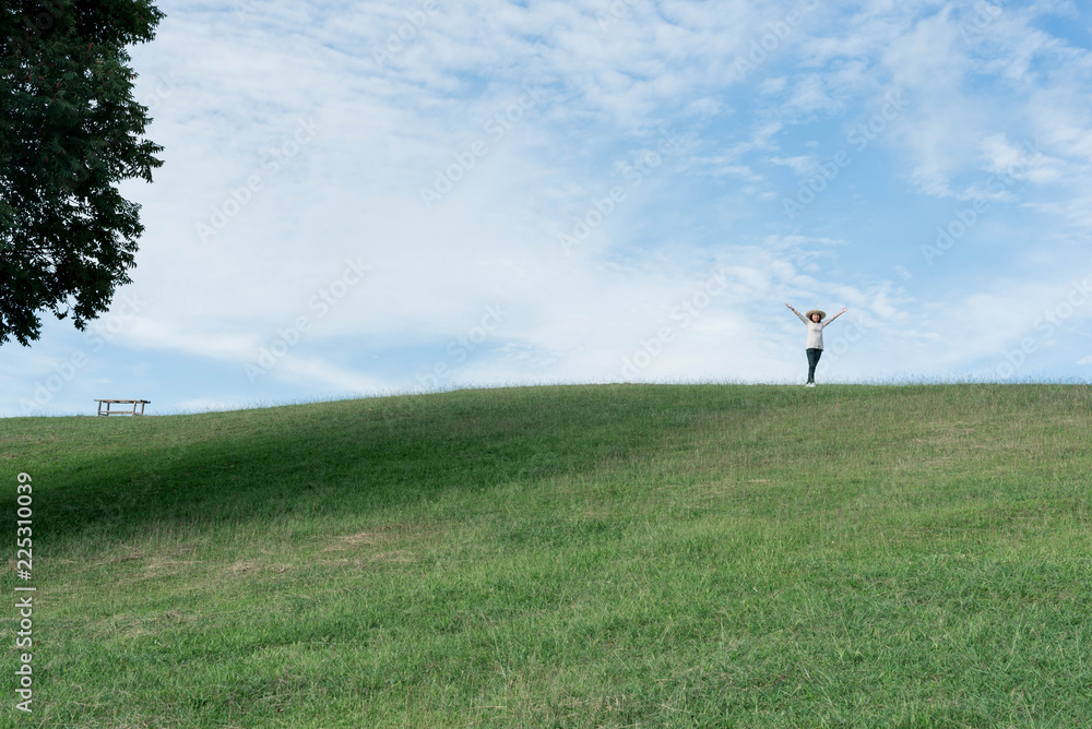 Standing woman raised her hands on the mountain, natural green and beautiful sky.