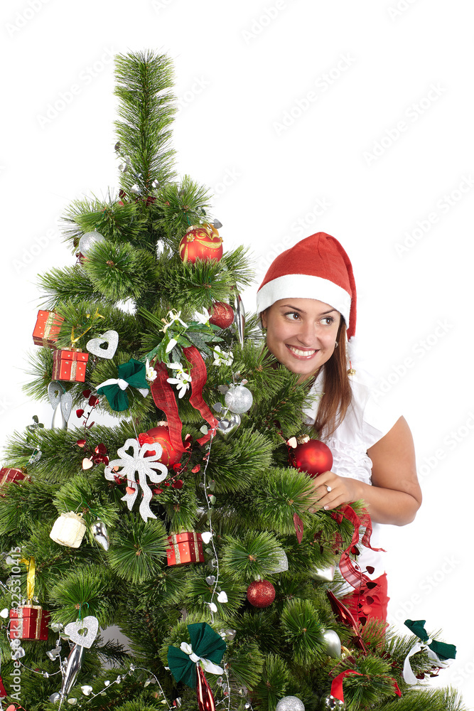 Beautiful smiling woman in Santa cap, behind the Christmas tree, isolated on white Beautiful smiling woman in Santa cap, behind the Christmas tree, isolated on white