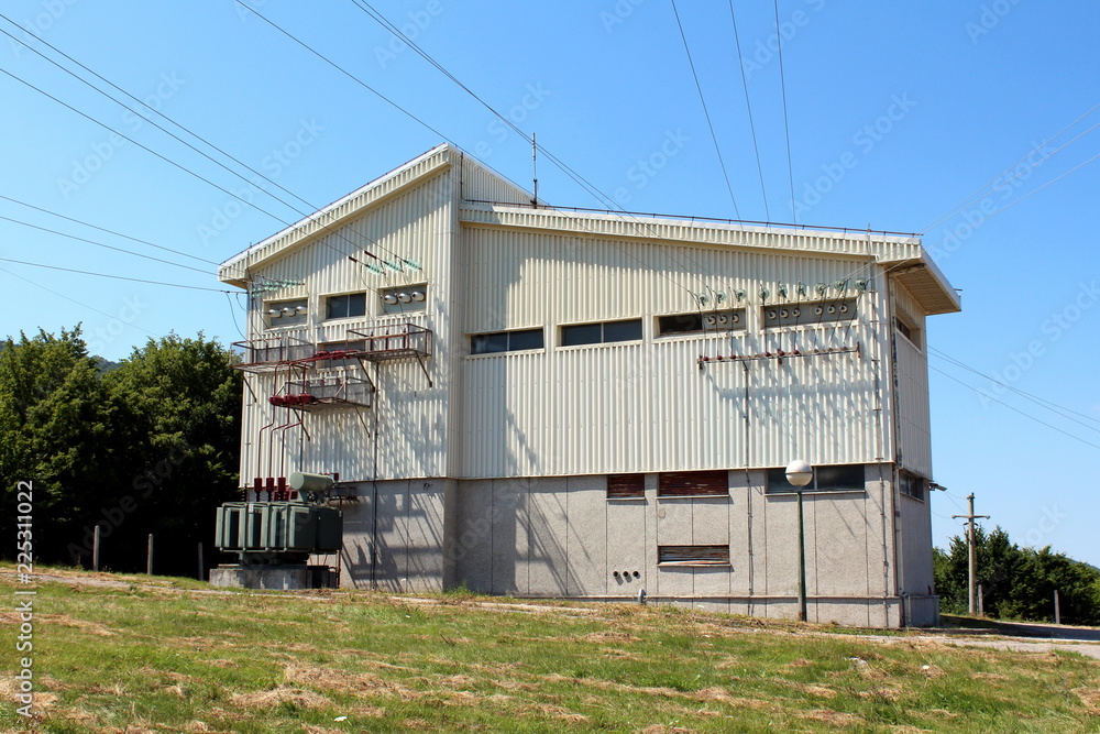 Large electrical company concrete white building coated with metal plates with multiple wires going in all direction connected with ceramic and glass insulators surrounded with uncut grass and forest Large electrical company concrete white building coated with metal plates with multiple wires going in all direction connected with ceramic and glass insulators surrounded with uncut grass and forest