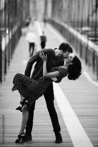 Love story in New York. Man and exotic woman dance with passion on the street with Brooklyn bridge behind them