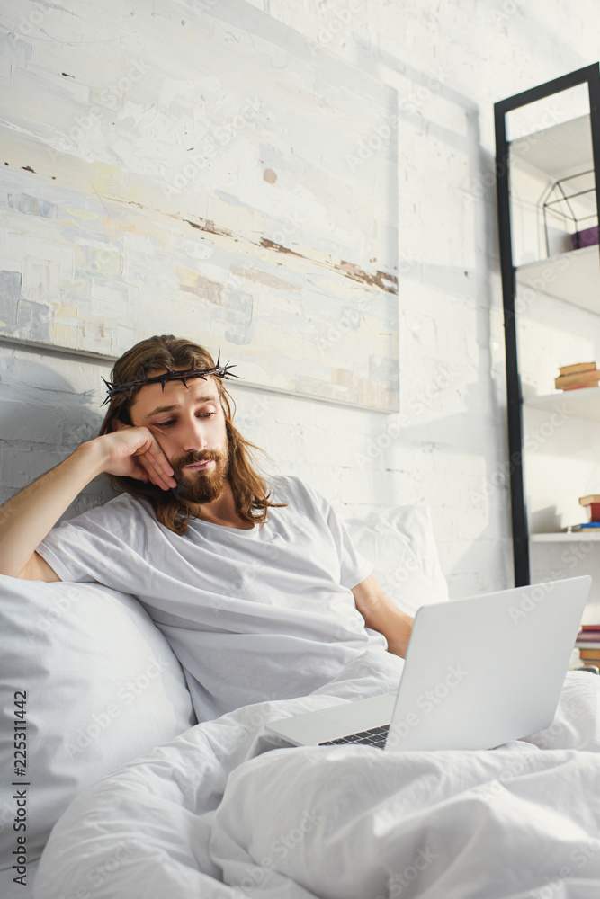skeptical Jesus using laptop in bed during morning time at home skeptical Jesus using laptop in bed during morning time at home