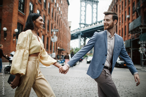 Love story in New York. Indian woman in bright yellow clothes and handsome American man hold each other hands walking around the New York © IVASHstudio