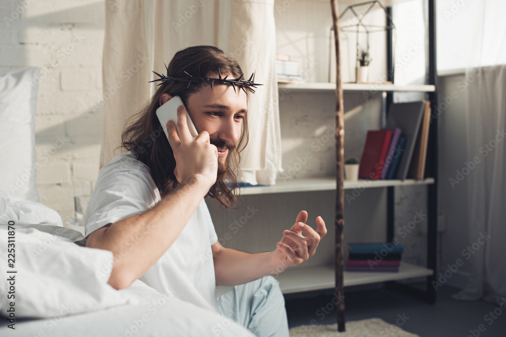 cheerful Jesus in crown of thorns talking on smartphone in bedroom at home cheerful Jesus in crown of thorns talking on smartphone in bedroom at home